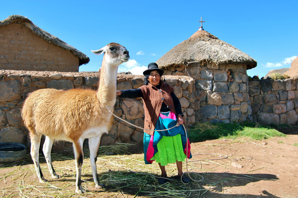 Frau mit Lama vor Haus in Peru